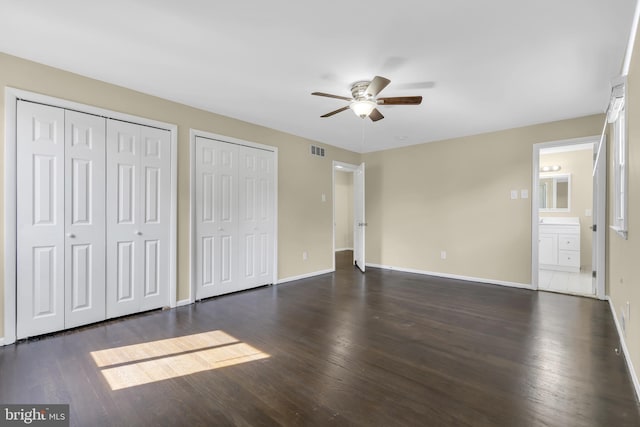 unfurnished bedroom featuring connected bathroom, ceiling fan, dark hardwood / wood-style floors, and multiple closets