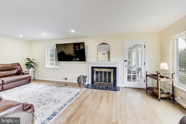 living room with a tile fireplace, light hardwood / wood-style floors, and a wealth of natural light