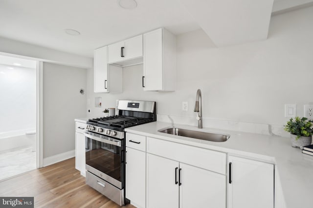 kitchen with gas range, sink, white cabinets, and light wood-type flooring