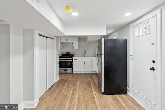 kitchen with appliances with stainless steel finishes, sink, white cabinets, and light hardwood / wood-style floors