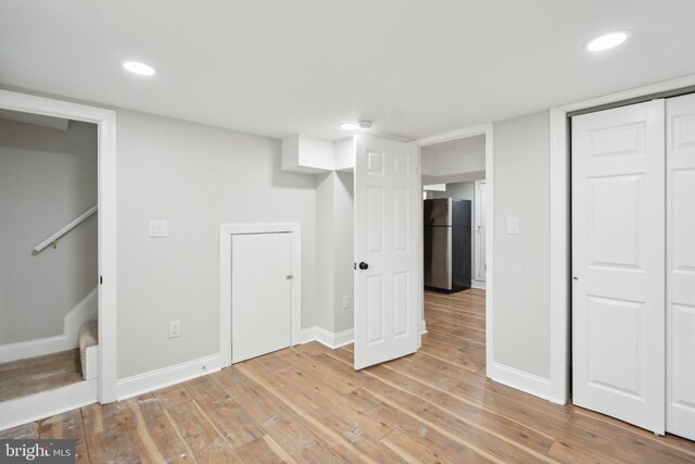 basement with stainless steel refrigerator and light hardwood / wood-style flooring