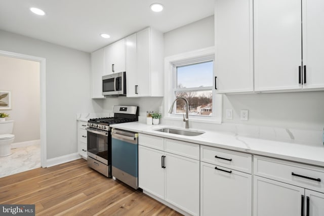 kitchen with sink, white cabinetry, stainless steel appliances, light stone counters, and light hardwood / wood-style floors