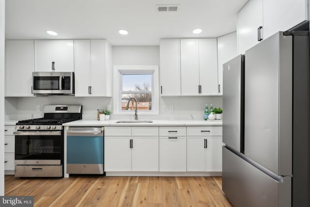 kitchen featuring appliances with stainless steel finishes, sink, light hardwood / wood-style flooring, and white cabinets