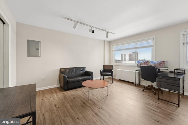 home office with rail lighting, electric panel, and light hardwood / wood-style flooring