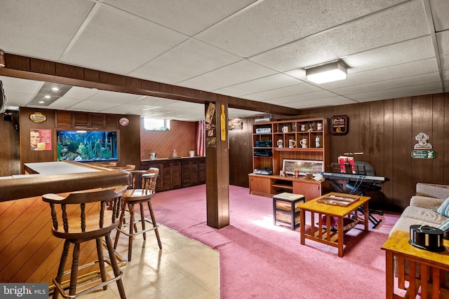 recreation room featuring wooden walls, carpet floors, a drop ceiling, and bar area