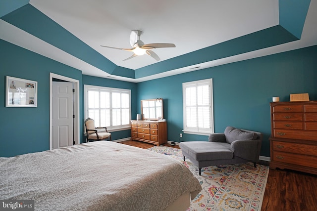 bedroom with a raised ceiling, wood-type flooring, and ceiling fan