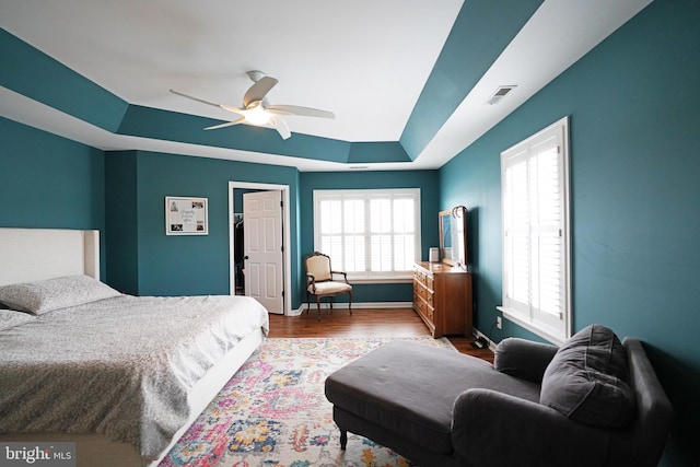 bedroom with multiple windows, hardwood / wood-style flooring, a raised ceiling, and ceiling fan