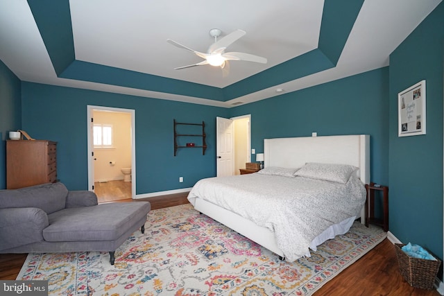 bedroom featuring connected bathroom, a tray ceiling, ceiling fan, and hardwood / wood-style flooring