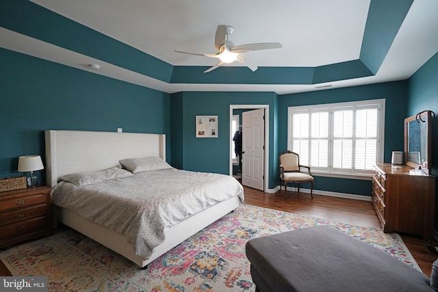 bedroom with wood-type flooring, ceiling fan, and a tray ceiling