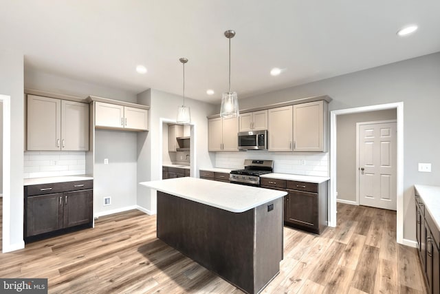 kitchen with appliances with stainless steel finishes, light wood-type flooring, tasteful backsplash, a kitchen island, and hanging light fixtures