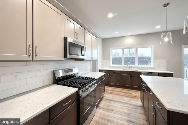 kitchen featuring sink, light stone counters, backsplash, decorative light fixtures, and appliances with stainless steel finishes