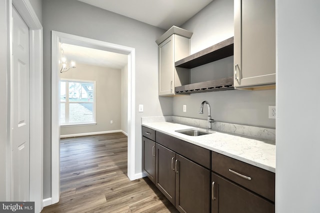 kitchen with light stone countertops, light wood-type flooring, dark brown cabinets, sink, and an inviting chandelier