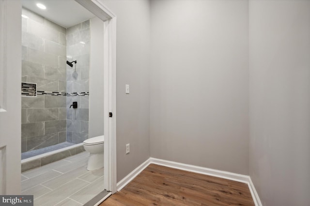 bathroom with hardwood / wood-style flooring, toilet, and a tile shower