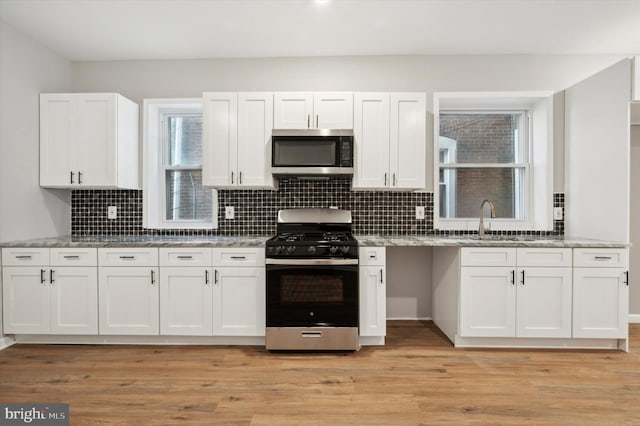 kitchen featuring light stone countertops, appliances with stainless steel finishes, light wood-type flooring, sink, and white cabinetry