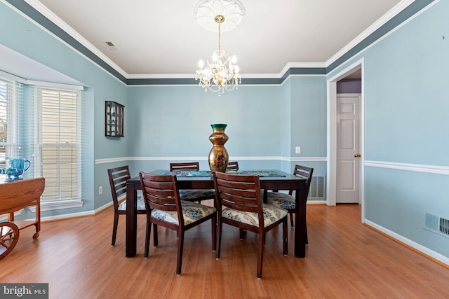 dining area featuring crown molding, a chandelier, and light hardwood / wood-style flooring