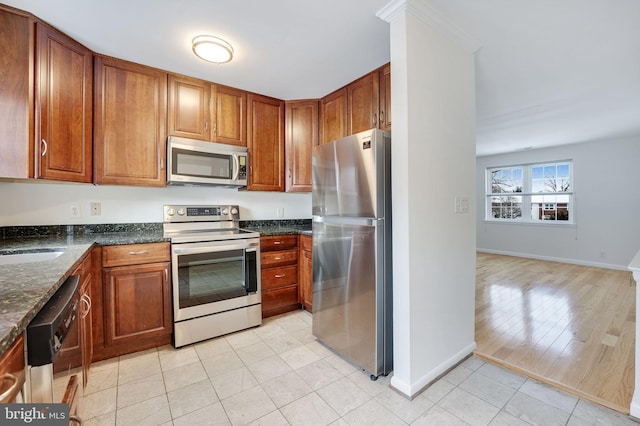 kitchen featuring sink, stainless steel appliances, dark stone counters, light hardwood / wood-style floors, and ornamental molding