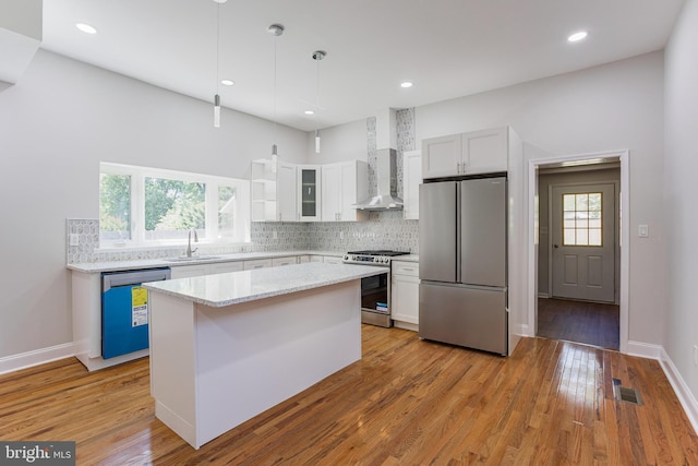 kitchen featuring white cabinetry, a center island, wall chimney exhaust hood, and stainless steel appliances