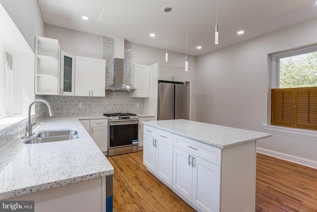 kitchen with a center island, white cabinets, wall chimney range hood, sink, and appliances with stainless steel finishes