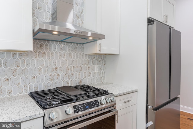 kitchen with white cabinets, appliances with stainless steel finishes, decorative backsplash, and wall chimney range hood