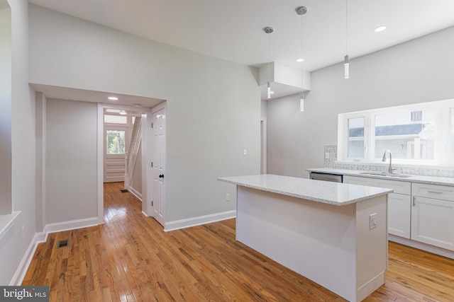 kitchen featuring light stone counters, sink, pendant lighting, white cabinets, and a center island