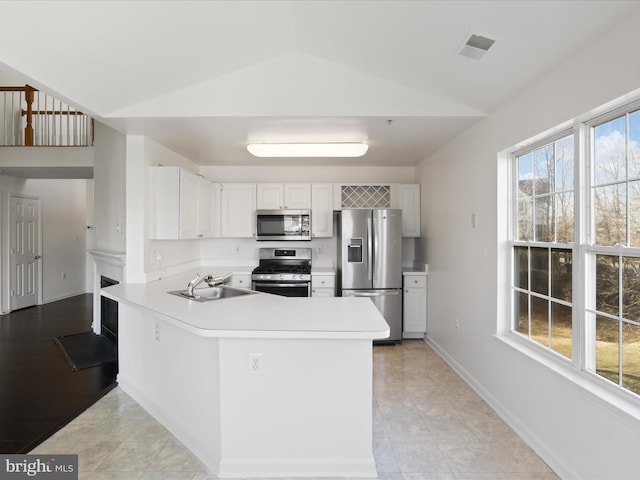 kitchen with sink, white cabinetry, stainless steel appliances, vaulted ceiling, and kitchen peninsula