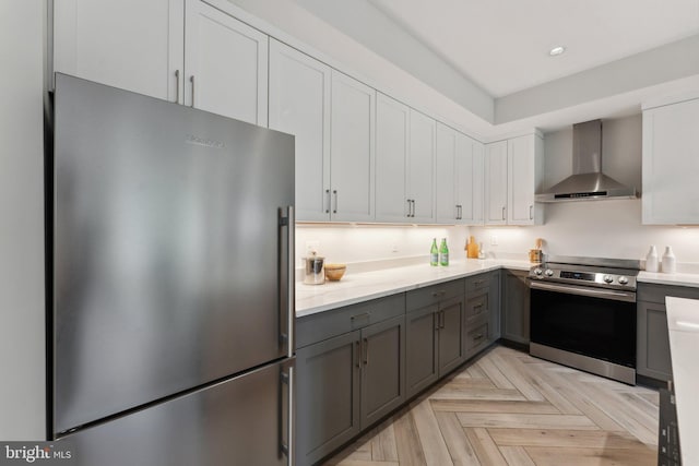 kitchen with stainless steel appliances, wall chimney range hood, light parquet flooring, gray cabinets, and white cabinetry