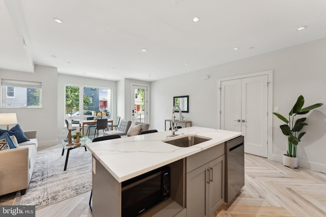 kitchen featuring sink, light stone counters, stainless steel dishwasher, an island with sink, and light parquet flooring