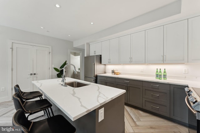 kitchen with sink, stainless steel appliances, light stone counters, a kitchen island with sink, and light parquet flooring