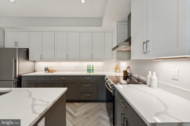 kitchen featuring light stone counters, stainless steel appliances, light parquet floors, wall chimney range hood, and white cabinets