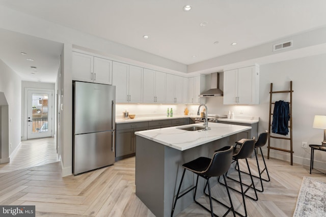 kitchen with light parquet floors, wall chimney range hood, sink, stainless steel fridge, and light stone counters