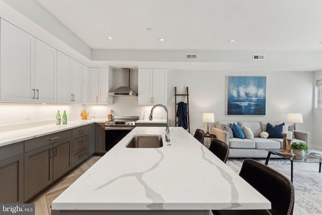 kitchen with sink, electric range, wall chimney exhaust hood, light stone counters, and white cabinetry