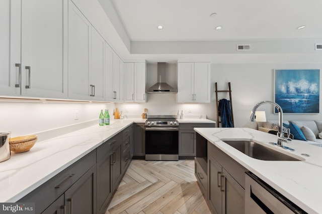 kitchen featuring white cabinets, wall chimney range hood, sink, light stone counters, and stainless steel appliances