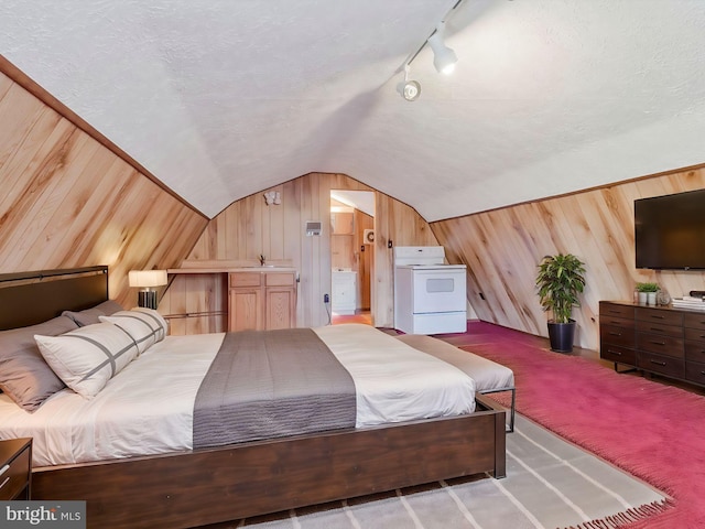 carpeted bedroom featuring ensuite bathroom, rail lighting, wooden walls, and vaulted ceiling