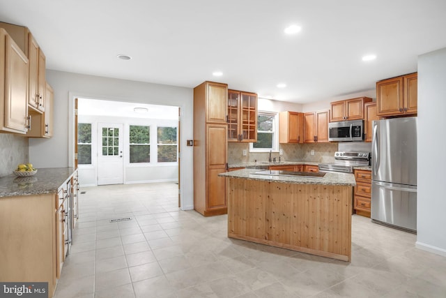 kitchen with appliances with stainless steel finishes, tasteful backsplash, a kitchen island, and light stone counters