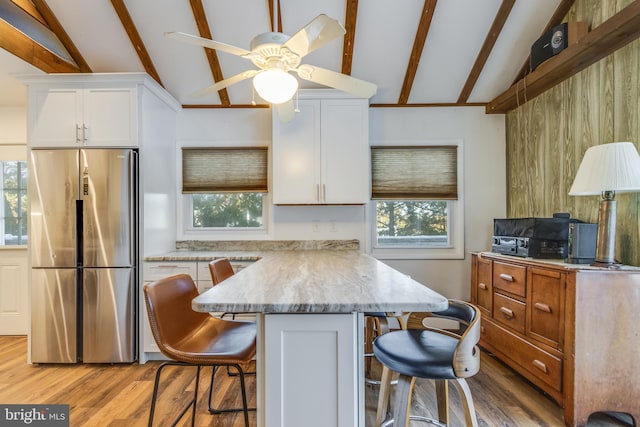 kitchen with a breakfast bar area, vaulted ceiling with beams, white cabinetry, light stone counters, and stainless steel fridge