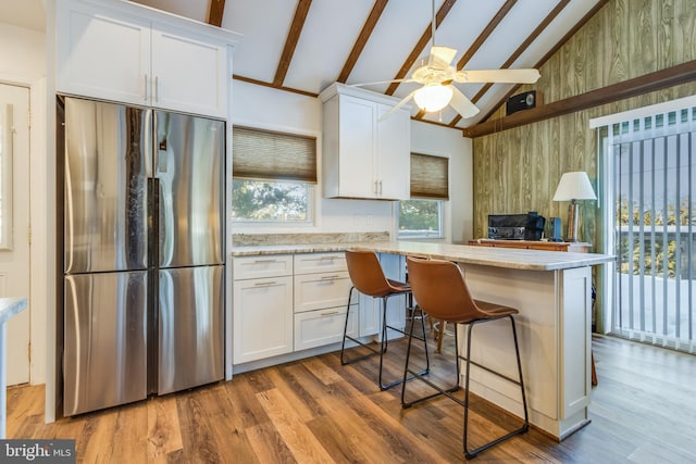 kitchen with a kitchen breakfast bar, white cabinets, stainless steel refrigerator, and kitchen peninsula