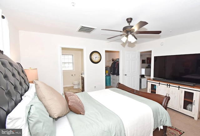 bedroom featuring connected bathroom, ceiling fan, a walk in closet, light carpet, and a closet