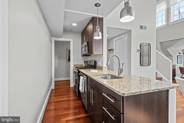 kitchen featuring sink, stainless steel appliances, light stone counters, pendant lighting, and dark wood-type flooring