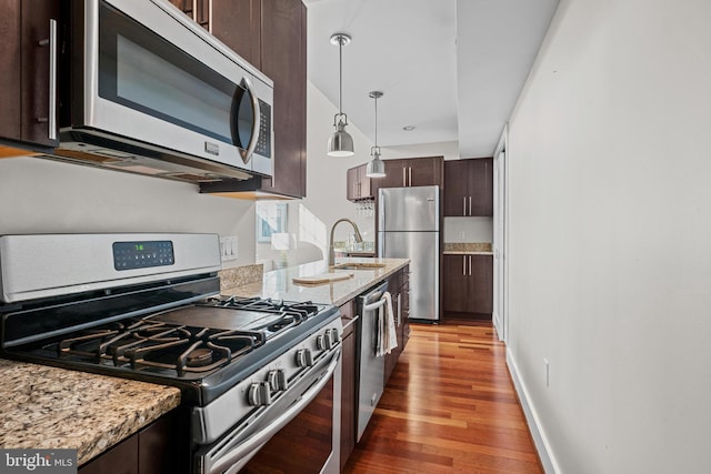 kitchen with stainless steel appliances, sink, light stone counters, dark brown cabinets, and pendant lighting