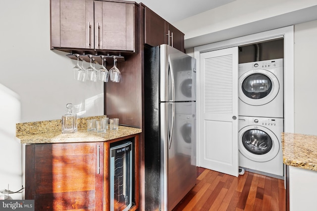 clothes washing area with wood-type flooring, stacked washer / drying machine, bar area, and wine cooler