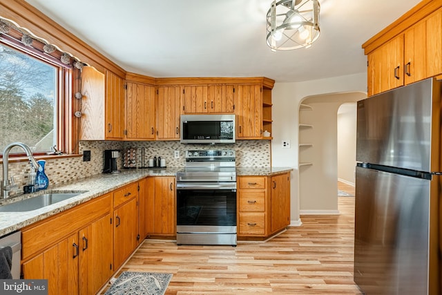 kitchen with sink, light stone counters, backsplash, light hardwood / wood-style floors, and appliances with stainless steel finishes