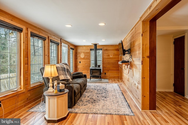 living room with light wood-type flooring, a wood stove, and wooden walls