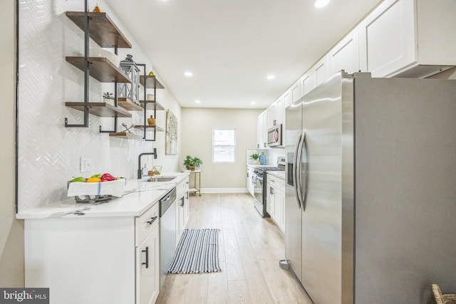 kitchen featuring sink, light wood-type flooring, tasteful backsplash, white cabinetry, and stainless steel appliances