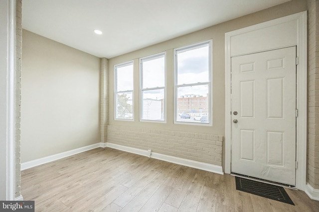 foyer entrance with light hardwood / wood-style flooring and brick wall