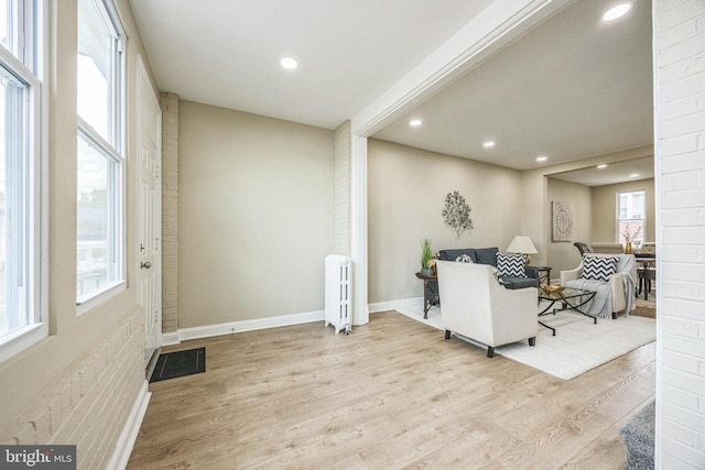 living room featuring light wood-type flooring, radiator, and brick wall