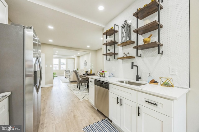 kitchen with white cabinets, sink, light stone countertops, light wood-type flooring, and appliances with stainless steel finishes