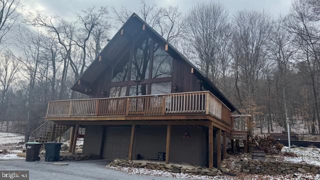 snow covered back of property with a wooden deck and a garage