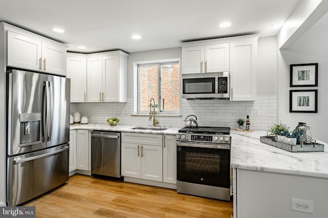 kitchen featuring appliances with stainless steel finishes, light wood-type flooring, light stone counters, sink, and white cabinets