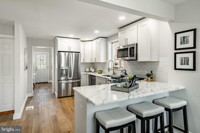 kitchen featuring white cabinets, sink, light stone countertops, kitchen peninsula, and stainless steel appliances