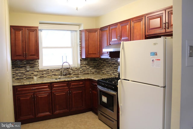 kitchen featuring stainless steel gas range, white fridge, light stone countertops, and sink